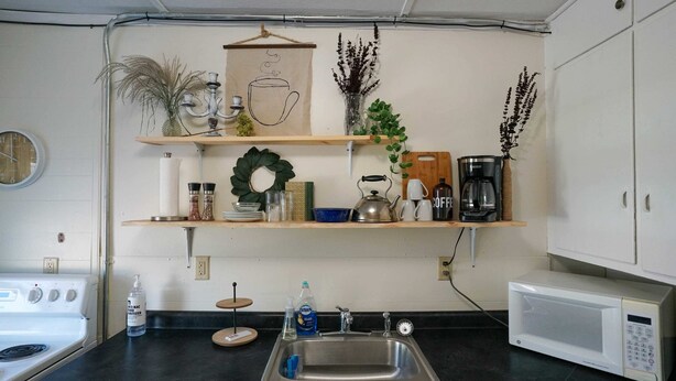 Una cocina con estufa, pileta y microondas. Hay estanterías con plantas y utensilios de cocina.