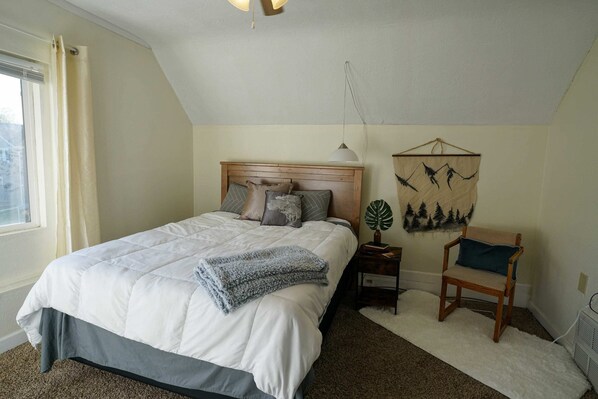 Une chambre à coucher avec un grand lit, une table de chevet, une chaise, une décoration murale et une fenêtre.