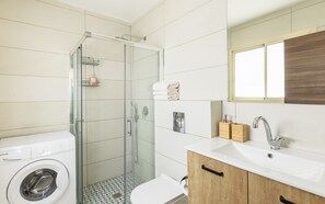 Enjoy a refreshing shower in the bathroom, featuring a glass-enclosed shower, a washing machine, and a vanity with sink and mirror.