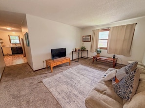 A living room with a television, a sofa, a coffee table, a rug, and a kitchen visible in the background. - 2 Bedroom Apartment near NDSU (APT 1) (Fargo)