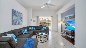 A living room with a sectional sofa, a coffee table, a TV on a stand, and a ceiling fan.