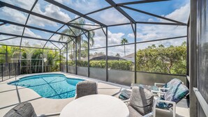 A covered outdoor area with a pool, seating, and a view of greenery.