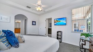 A bedroom with a bed, a ceiling fan, a TV, a window with bars, and a plant on a side table.