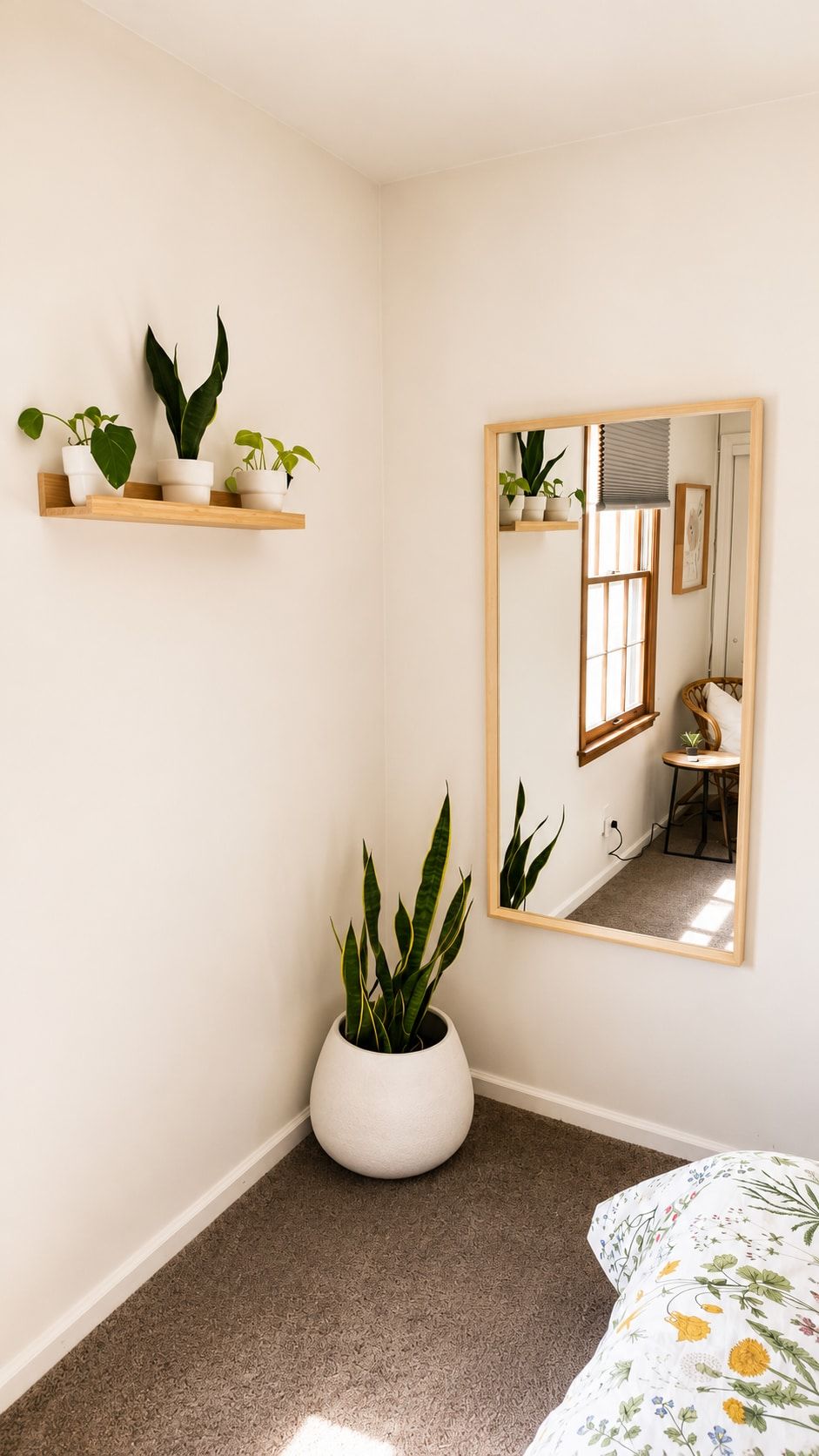 A room with a large mirror, a potted plant, and a bed with floral bedding.