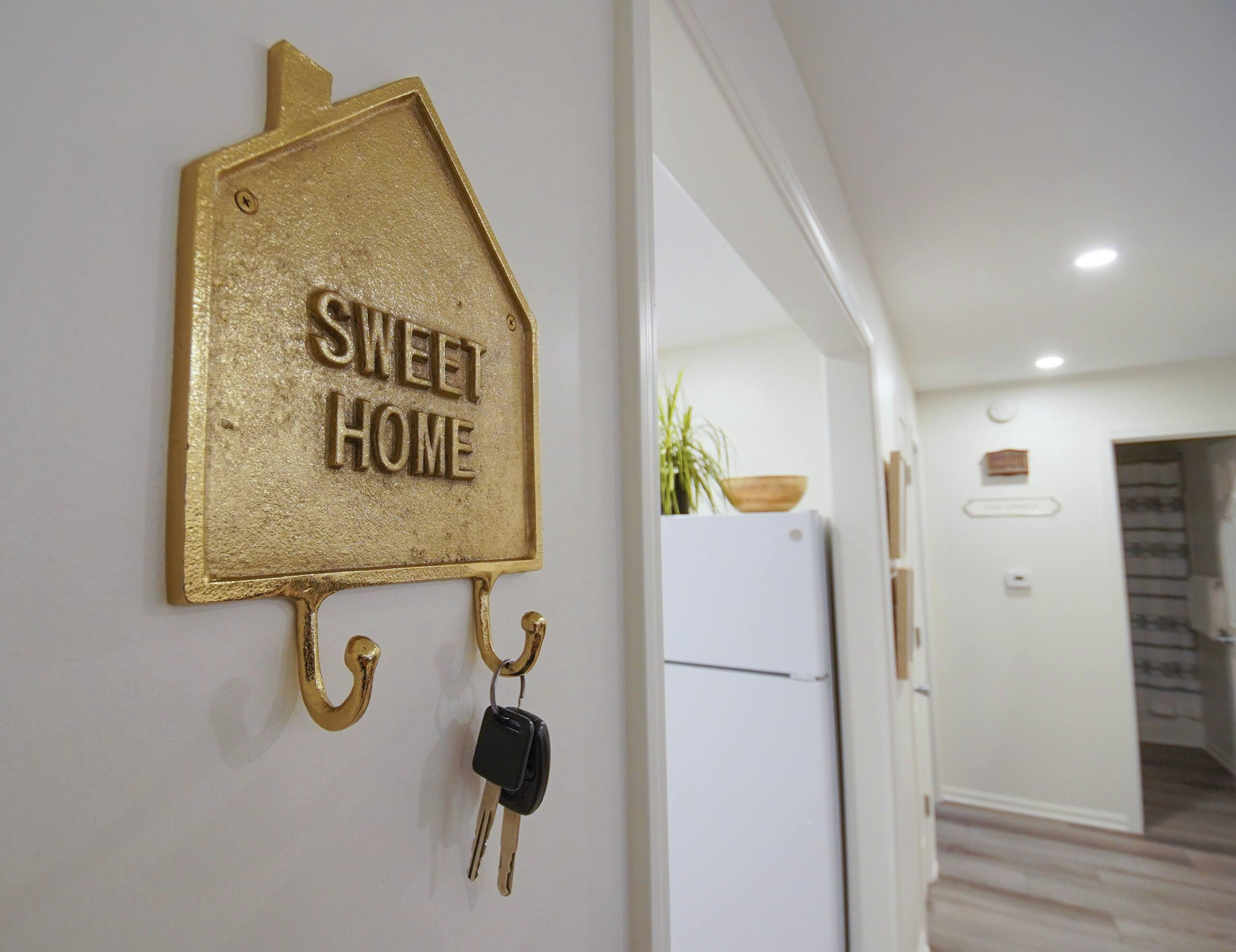 Un porte-clés mural orné d’une plaque en forme de maison sur laquelle on peut lire « SWEET HOME », et auquel est accroché un trousseau de clés.
