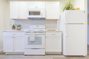 Eine Küche mit weißen Schränken, einer Mikrowelle, einem Backofen und einem Kühlschrank.