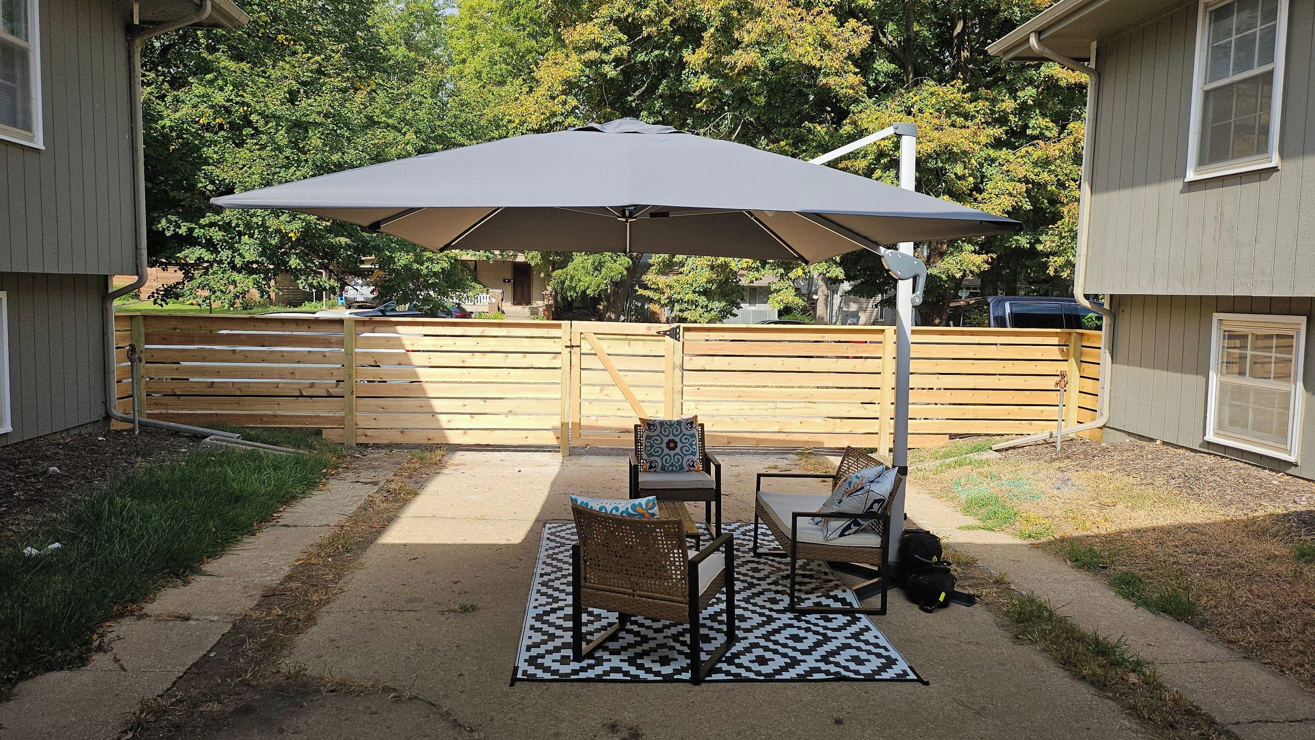 Une terrasse extérieure avec une table et des chaises, un grand parasol et un tapis à motifs.