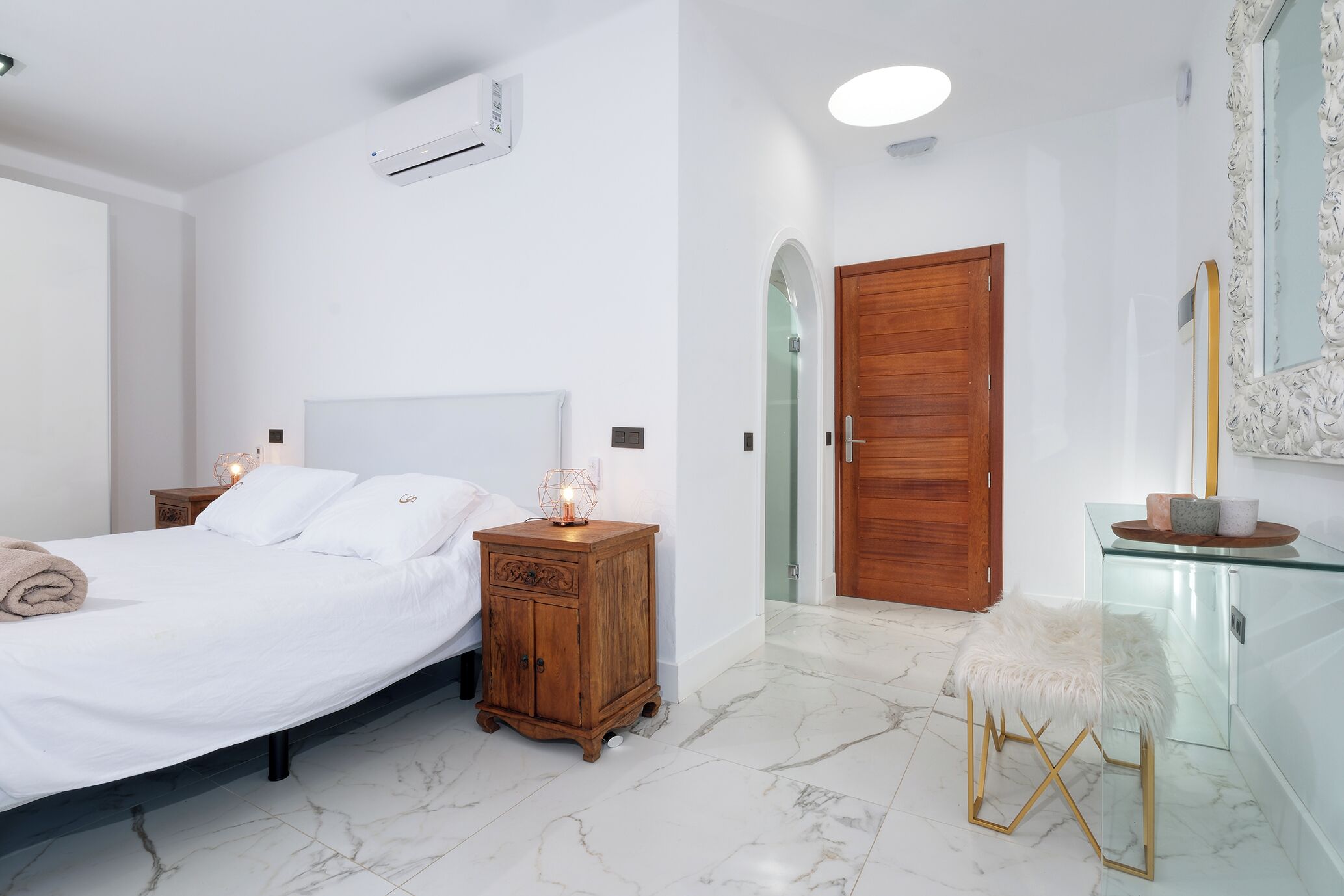 Een slaapkamer met een bed, houten nachtkastjes, een glazen kast en een marmeren vloer.
