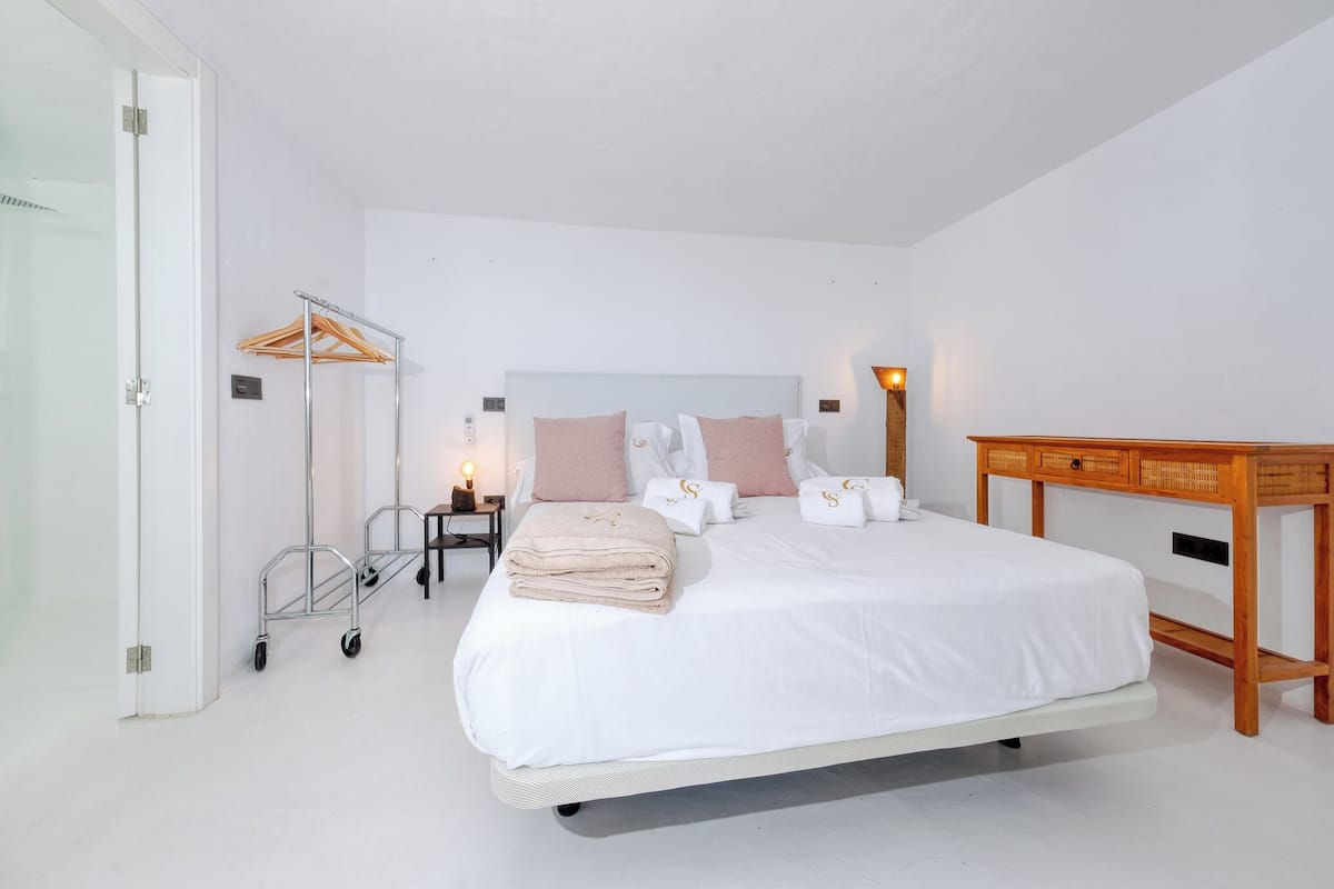 A neatly arranged bedroom with a bed, bedside tables, a wooden nightstand, and a wall-mounted towel rack.