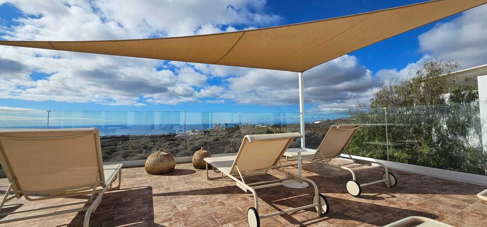 Eine Terrasse mit Liegestühlen, Sonnensegel und Meerblick.