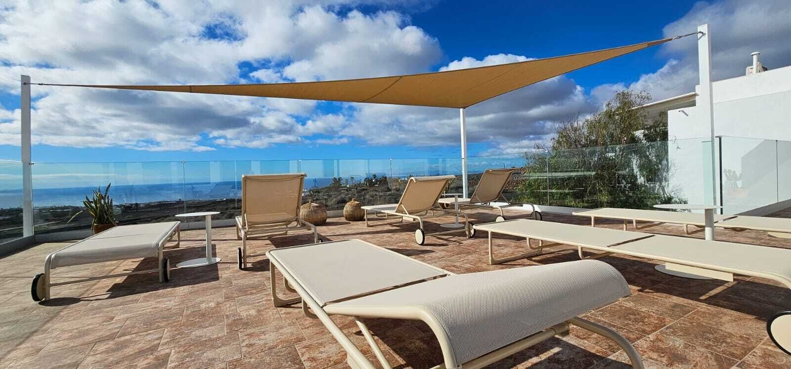 A rooftop terrace with lounge chairs, a large canopy, and a clear view of the ocean.