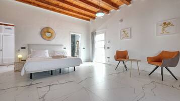 A spacious bedroom with a large bed, a wooden ceiling, and a marble floor. There are two chairs and a small table in the room.