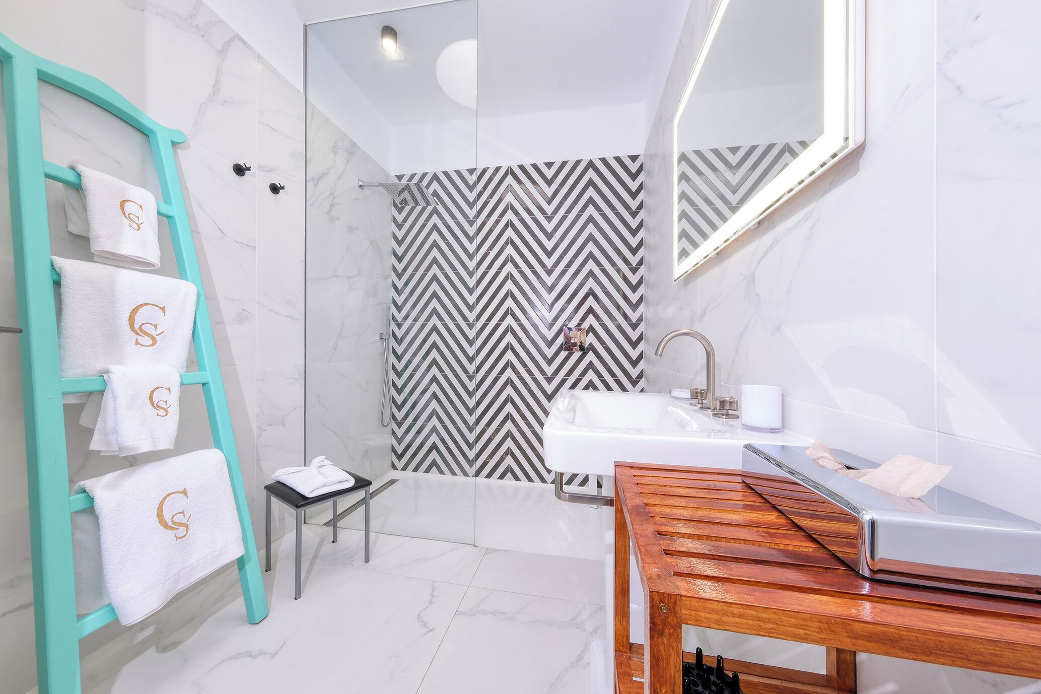 Un baño moderno con un perchero azul turquesa, una ducha con pared de diseño en blanco y negro con patrón de chevron, un lavamanos blanco y un mueble de tocador de madera.