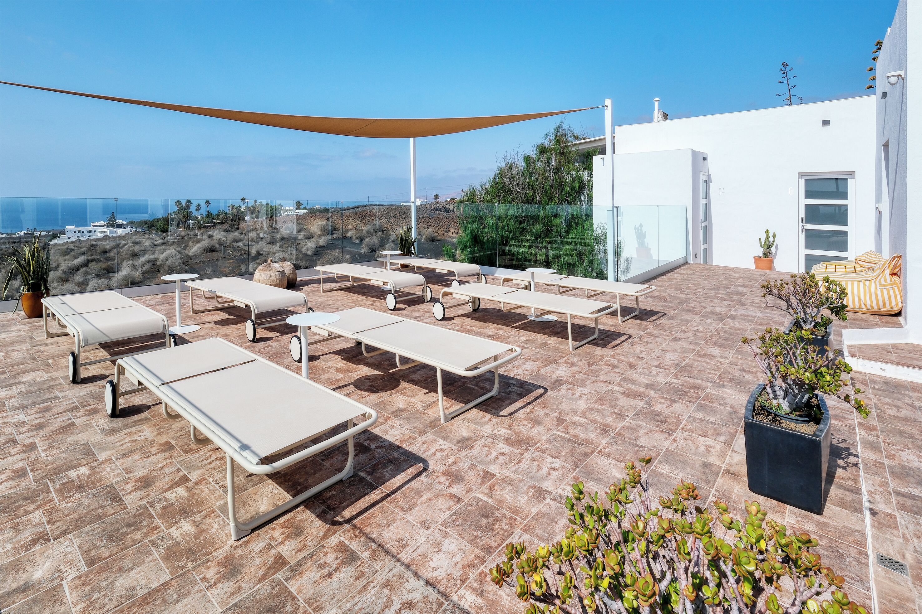 A rooftop terrace with sun loungers, a large shade sail, and potted plants.