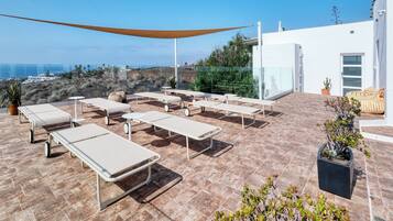 A rooftop terrace with sun loungers, a large shade sail, and potted plants.