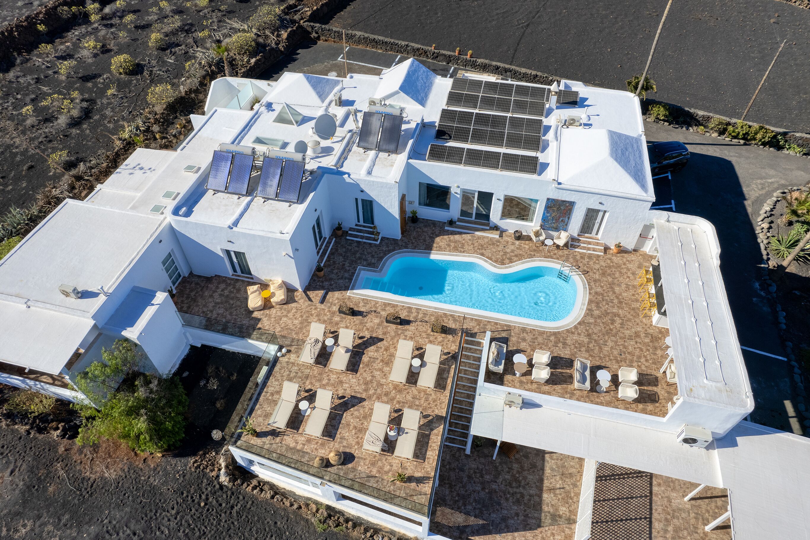 An aerial view of a modern resort with a swimming pool, sun loungers, and solar panels.