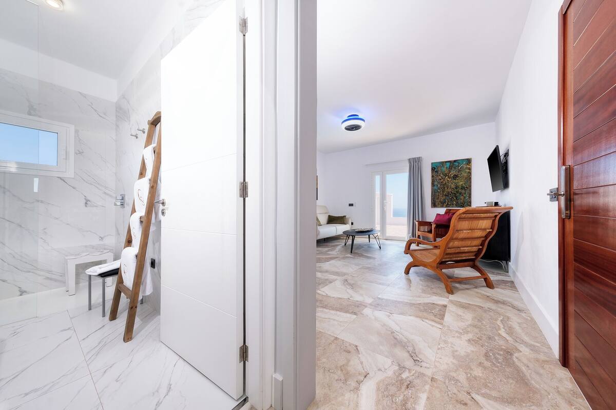 A modern bathroom with marble tiles, a wooden ladder, and a white bench.