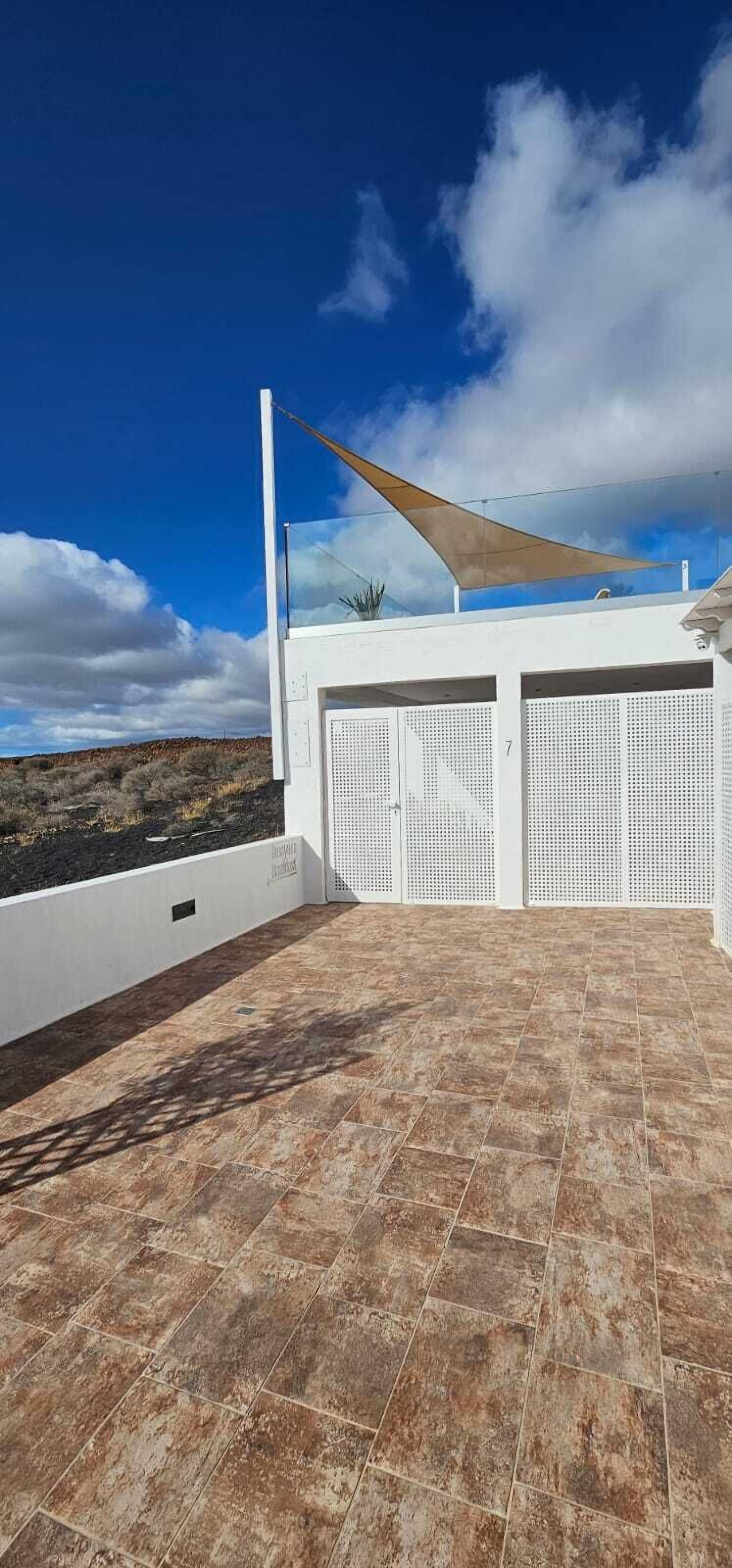 A rooftop terrace with a view of the landscape, a white building, and a large sunshade.