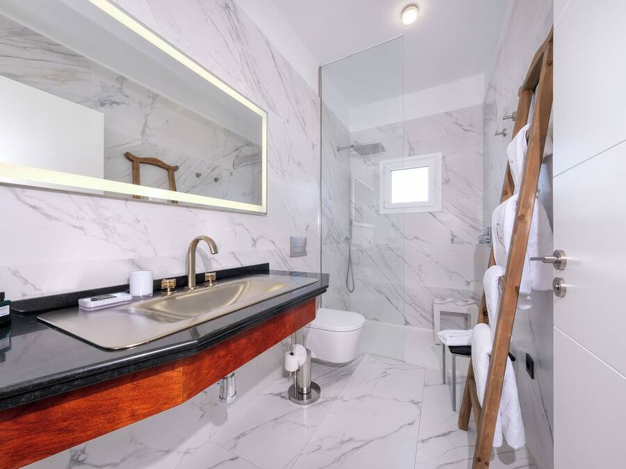 Un baño moderno con lavamanos de mármol, un espejo grande, cabina de ducha con paredes de vidrio y una escalera de madera.