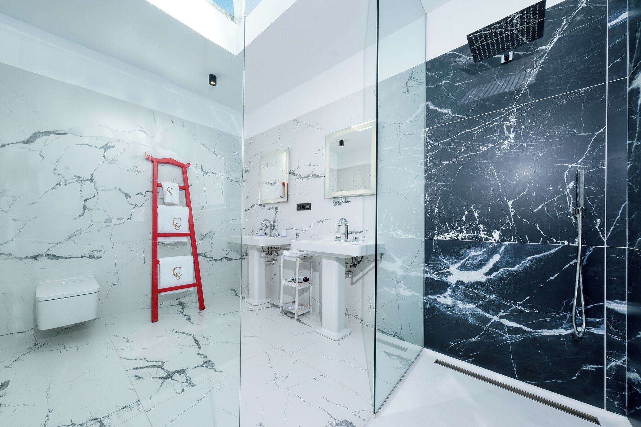 Un baño moderno con paredes de mármol blanco, cabina de ducha con mampara de vidrio y una escalera roja.