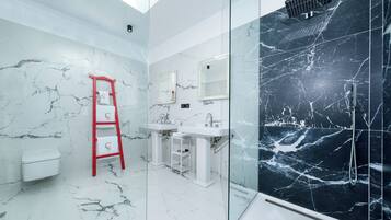Un baño moderno con paredes de mármol blanco, cabina de ducha con mampara de vidrio y una escalera roja.