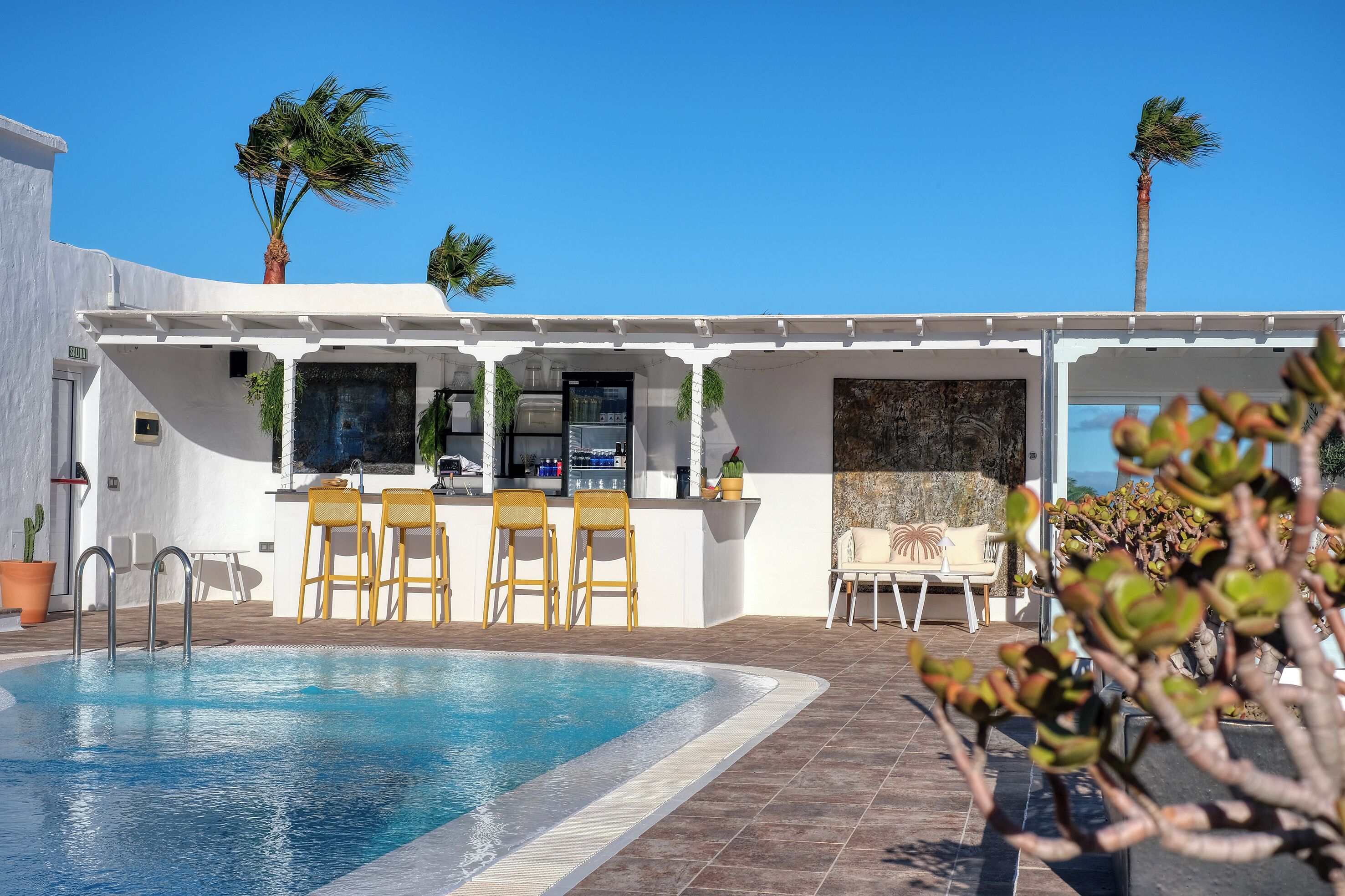 Zona de piscina con bar, asientos y palmeras.