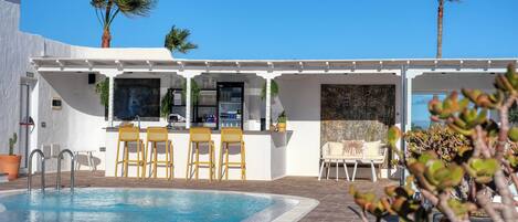 A poolside area with a bar, seating, and palm trees.