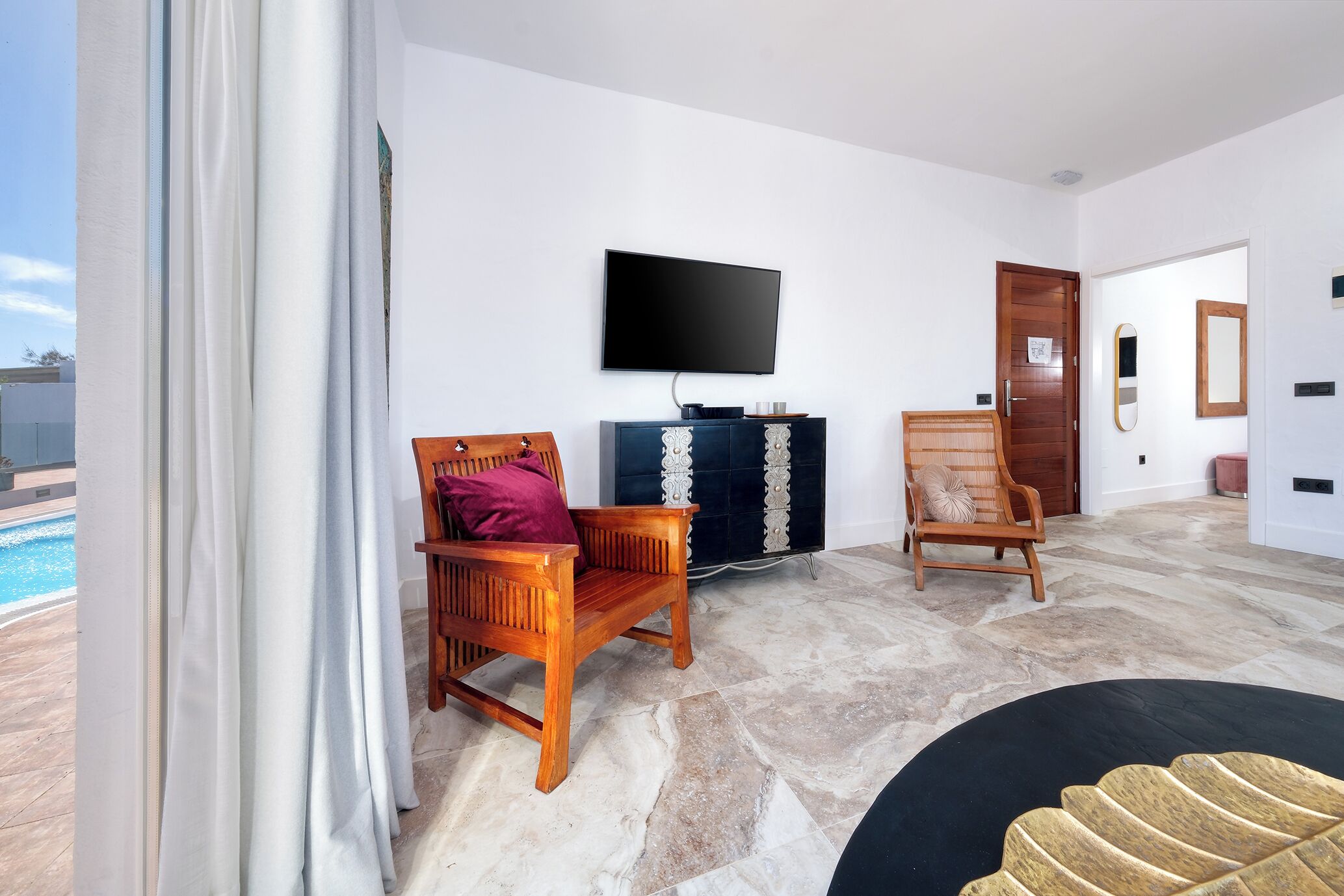 Ein geräumiges Wohnzimmer mit großem Fernseher, zwei Holzstühlen, einem dunkelblauen Schrank und einem Pool, der durch das Fenster sichtbar ist.