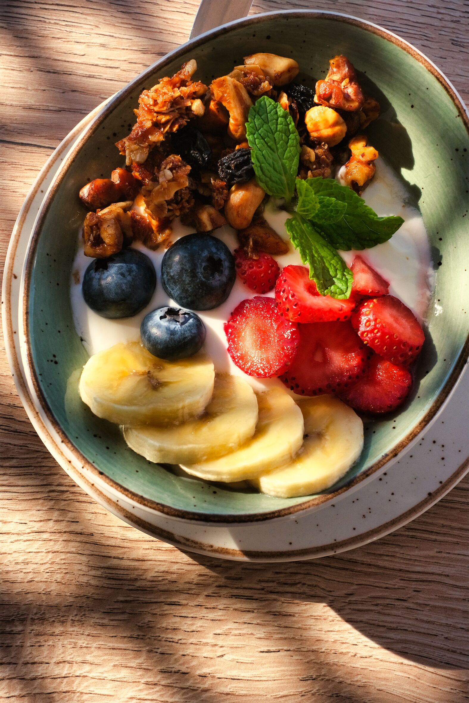 Una ciotola di yogurt con frutta e noci su un tavolo di legno.