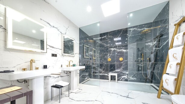 Un baño moderno con suelo de mármol, cabina de ducha con paredes de cristal y tocador con detalles dorados.