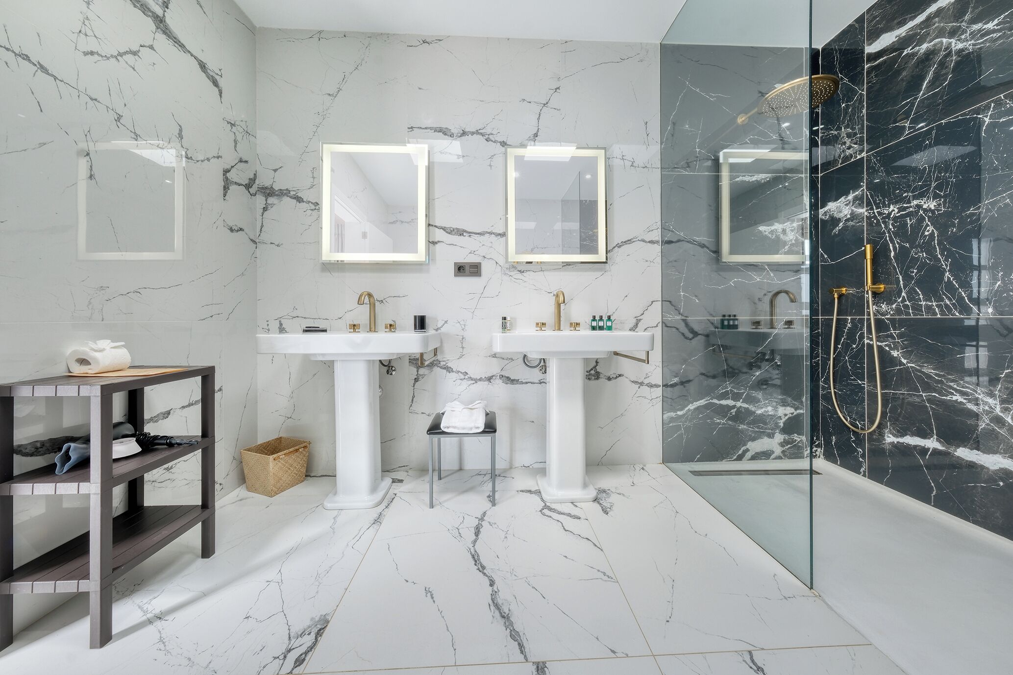 Un baño moderno con paredes de mármol, dos lavamanos y una ducha con mampara de vidrio.