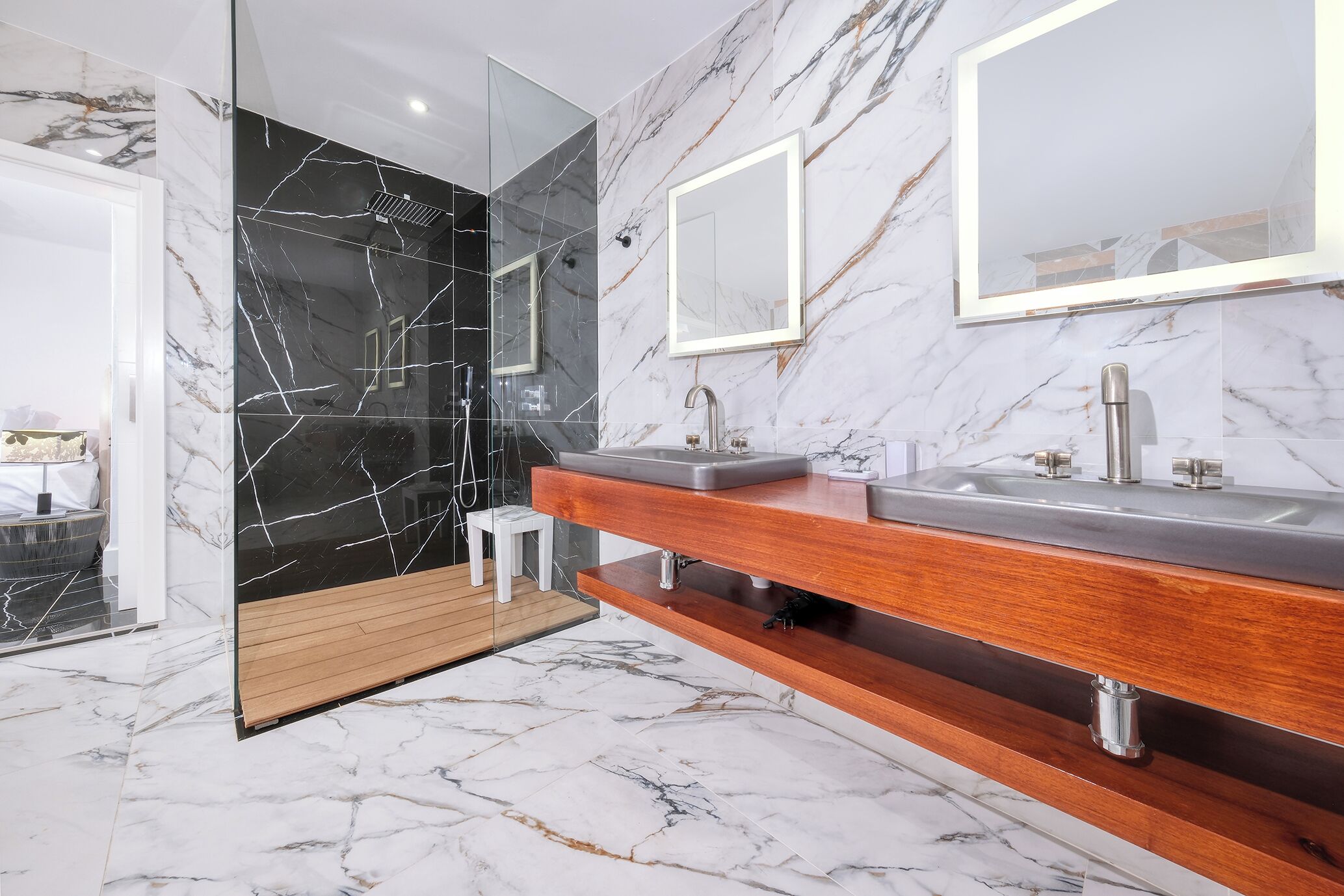 A modern bathroom with marble flooring, a wooden vanity, and a glass-enclosed shower area.