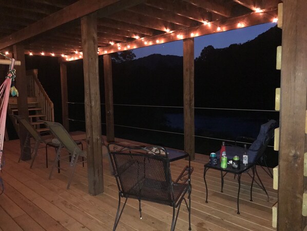 An outdoor deck with wooden flooring, metal chairs, a table with drinks, and string lights.
