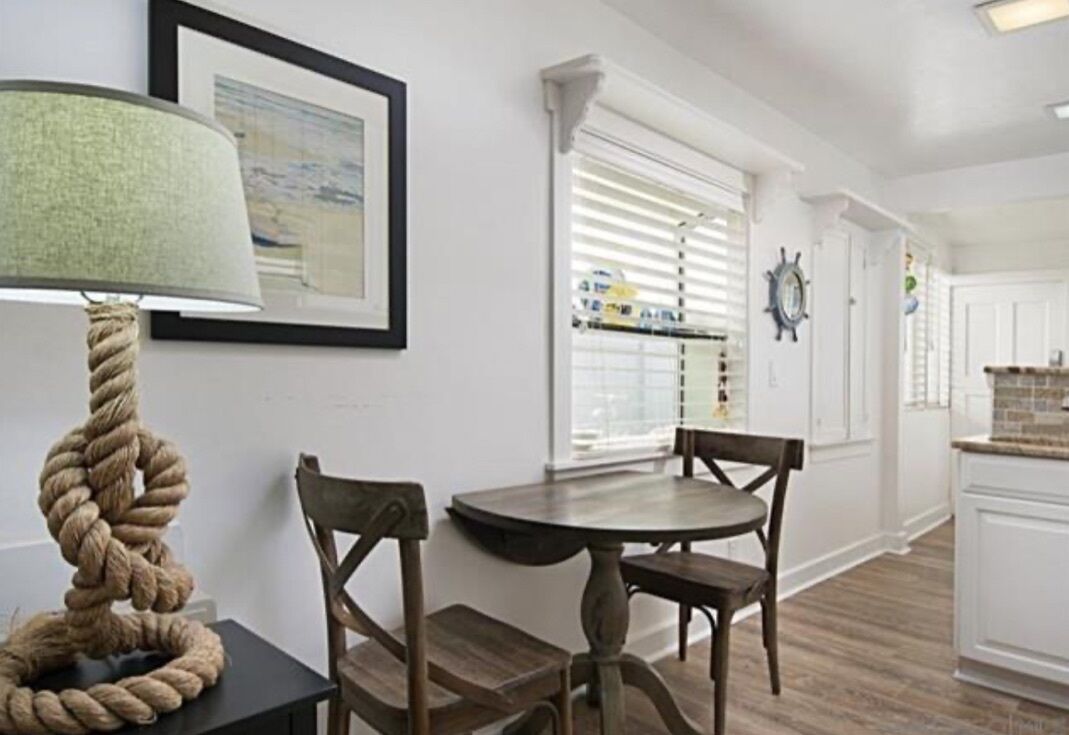 Een eethoek met een ronde tafel en twee stoelen, een touwlantaarn en een ingelijst beeld aan de muur.
