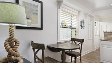 Een eethoek met een ronde tafel en twee stoelen, een touwlantaarn en een ingelijst beeld aan de muur.