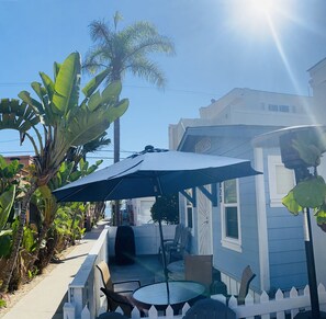 A patio with a table and chairs under a large umbrella, surrounded by lush greenery and a white fence. - Charming Beach Bungalow steps from the Ocean & Bay (San Diego)