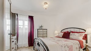 Un dormitorio con cama, cómoda, mesita de noche y ventana con cortinas.