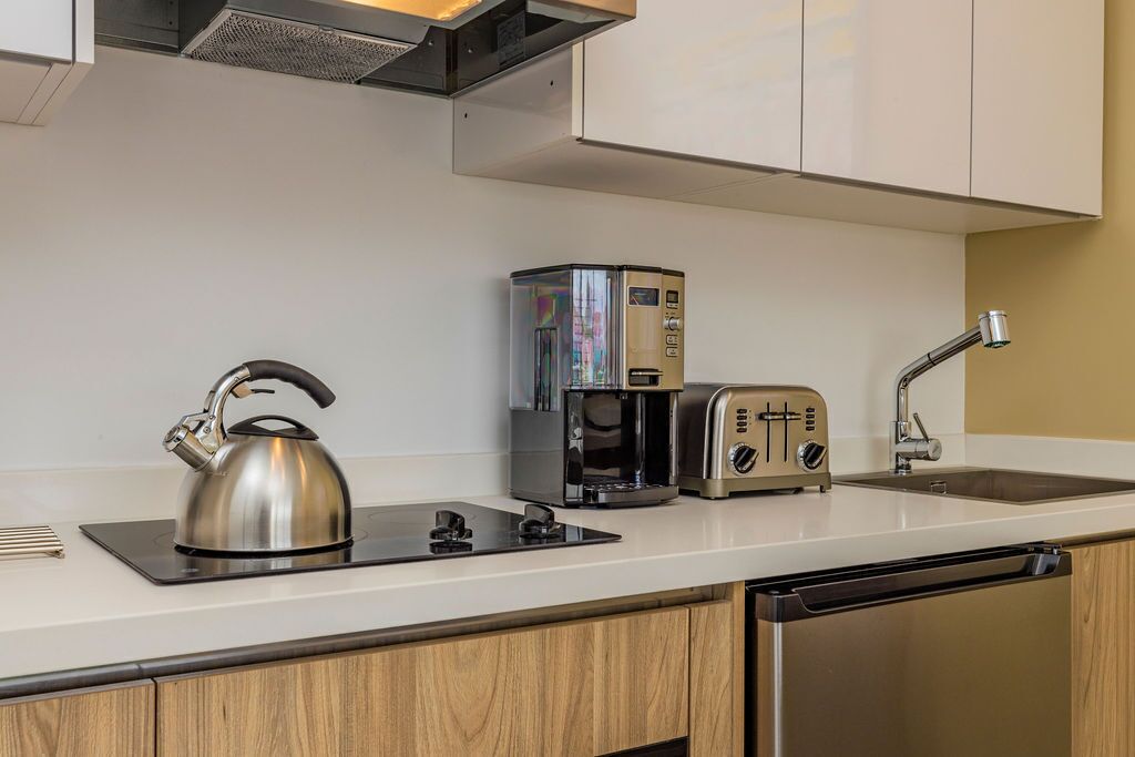 Eine moderne Küche mit Wasserkocher, Kaffeemaschine und Toaster auf der Arbeitsfläche, einem Spülbecken und Holzschränken.