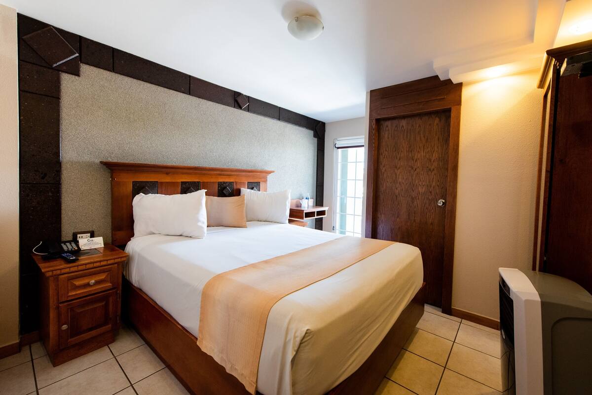Una habitación de hotel con una cama grande, cabecera de madera, mesitas de noche, un escritorio y un armario.