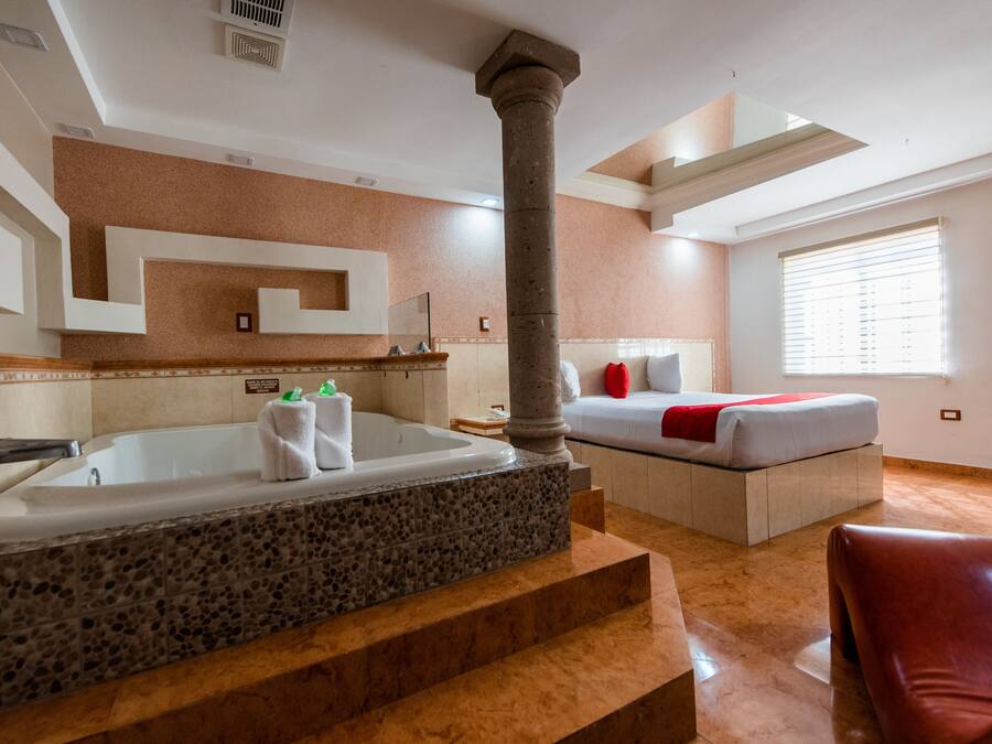 Quarto de hotel moderno com uma banheira grande, uma cama com manta vermelha e piso de mármore.