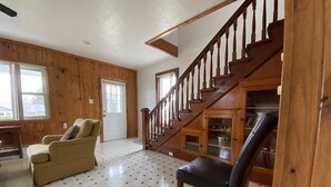 A spacious living room with a wooden staircase, a beige sofa, a black leather chair, and a tiled floor. - Sundown Lodge in McMillan MI (McMillan)