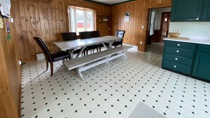 A wooden-paneled room with a dining table, chairs, and a kitchen area with teal cabinets. - Sundown Lodge in McMillan MI (McMillan)