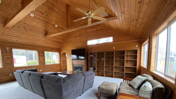 A spacious living room with a large gray sectional sofa, a wooden coffee table, and a fireplace. There are multiple bookshelves and a television mounted on the wall. - Sundown Lodge in McMillan MI (McMillan)