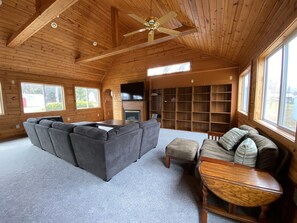 A spacious living room with a large gray sectional sofa, a wooden coffee table, and a fireplace. There are multiple bookshelves and a television mounted on the wall. - Sundown Lodge in McMillan MI (McMillan)