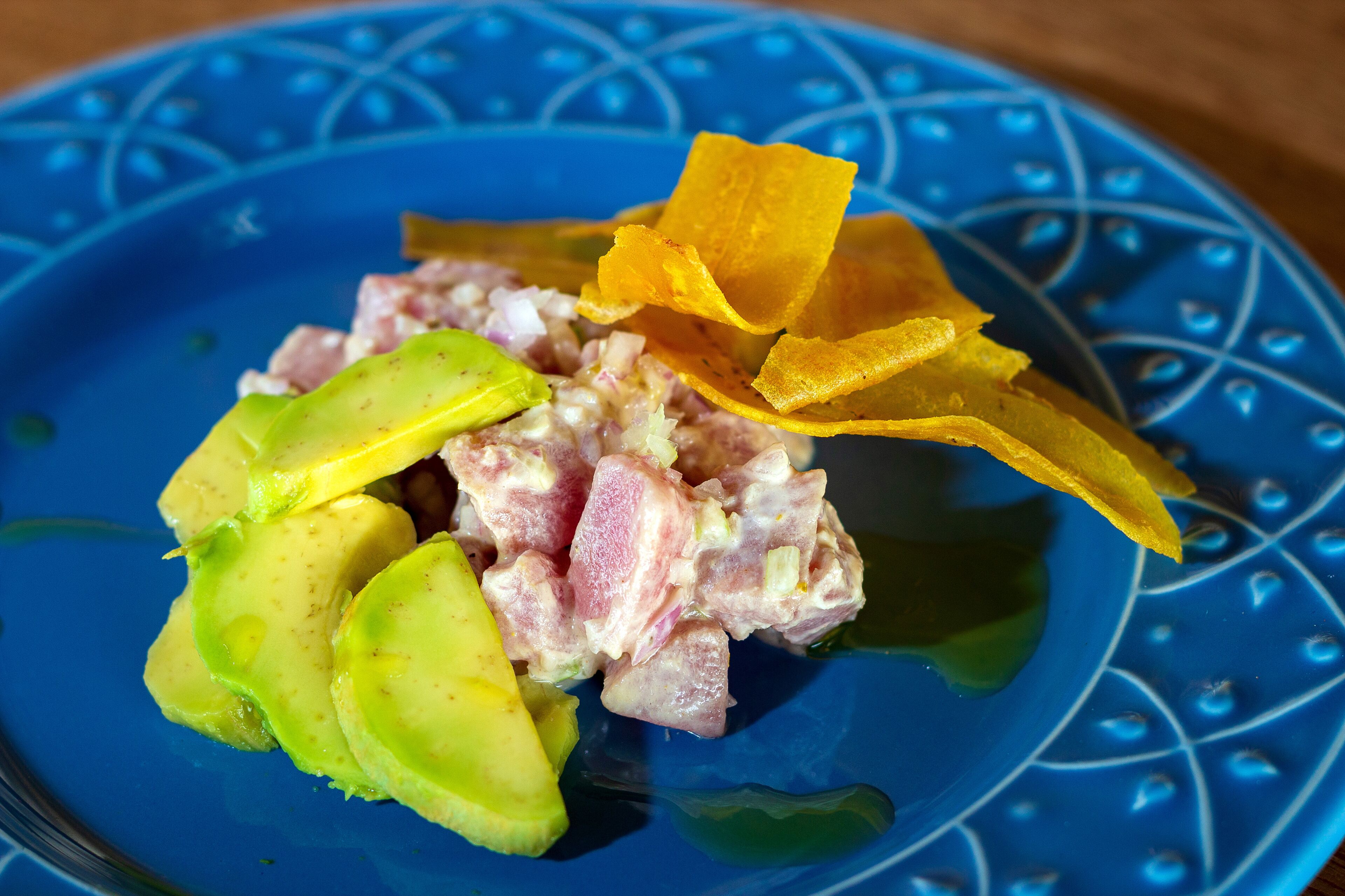 A blue plate with a dish of diced meat and avocado slices, accompanied by yellow chips.