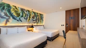 A hotel room with two beds, a desk, a chair, a large leaf-patterned mural, and a wooden door.