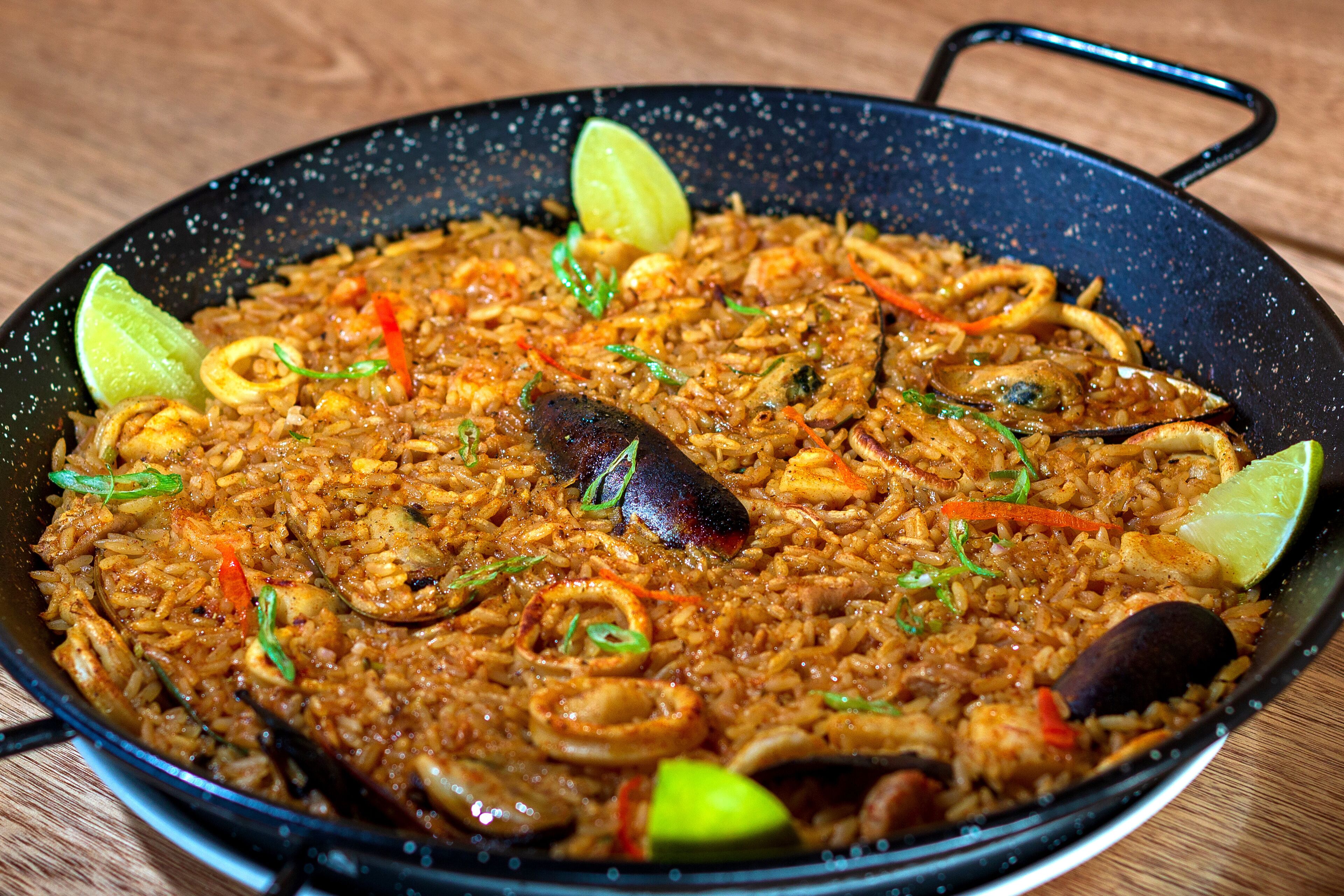 Eine große Pfanne mit einem Reisgericht, garniert mit Limette, Frühlingszwiebeln und roten Paprika.