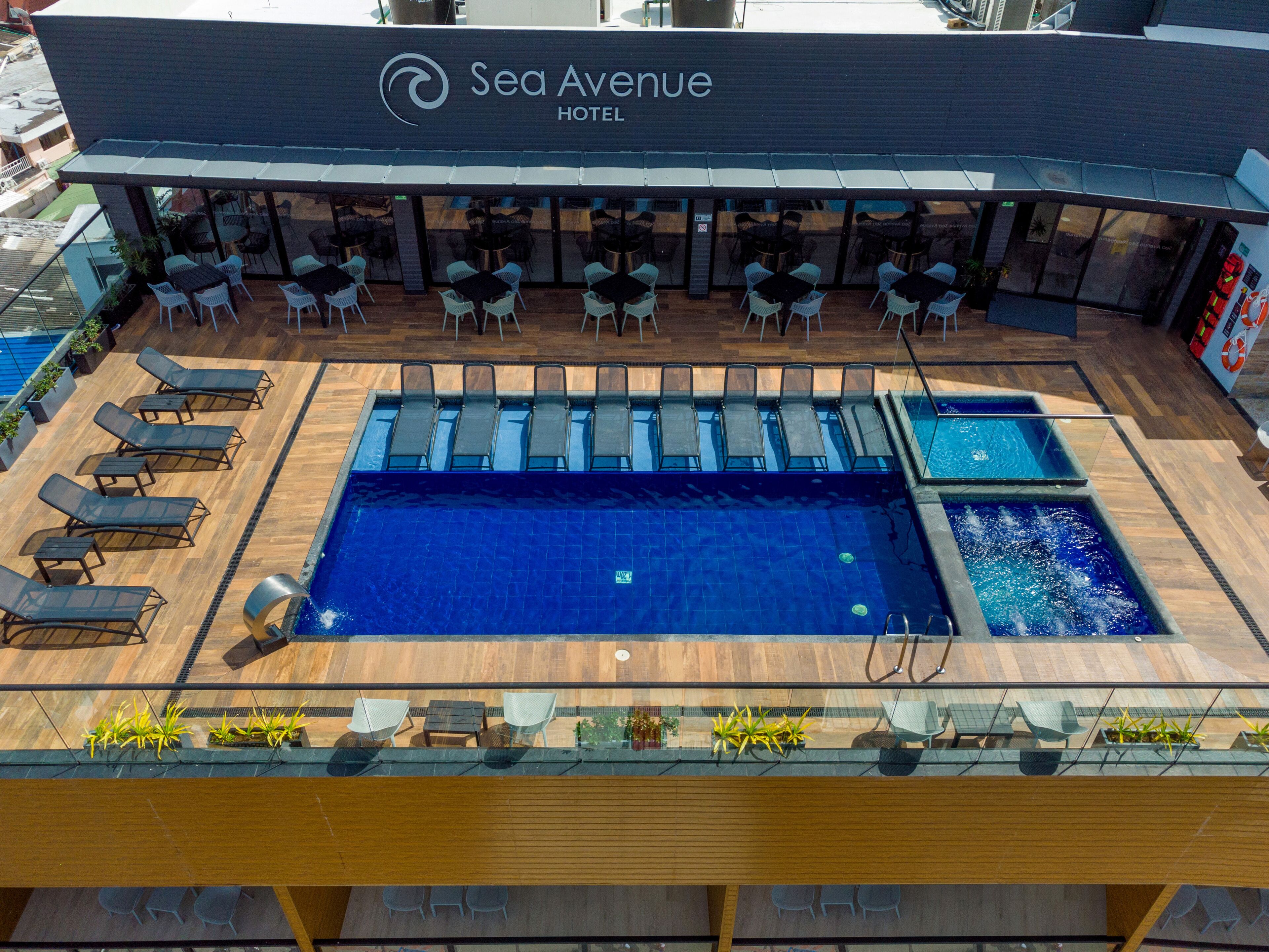 Une piscine sur le toit d’un hôtel situé sur Sea Avenue, avec des chaises longues, des tables et une plus petite piscine.
