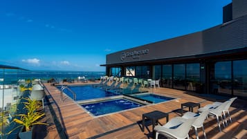 A Sea Avenue Hotel rooftop pool with clear views of the ocean, lounge chairs, and a glass balustrade.