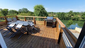 Une terrasse en bois avec une table et des chaises, un barbecue et une vue sur une rivière.